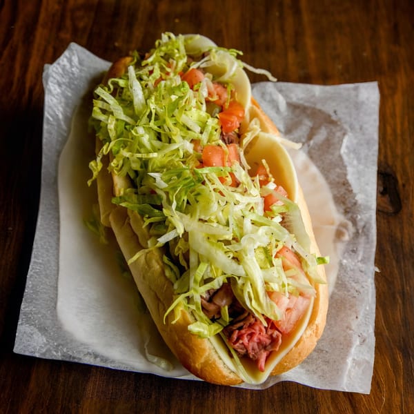 A Nicolini House of Pizza sub sandwich with meat, cheese, lettuce, and tomatoes on a wooden table.