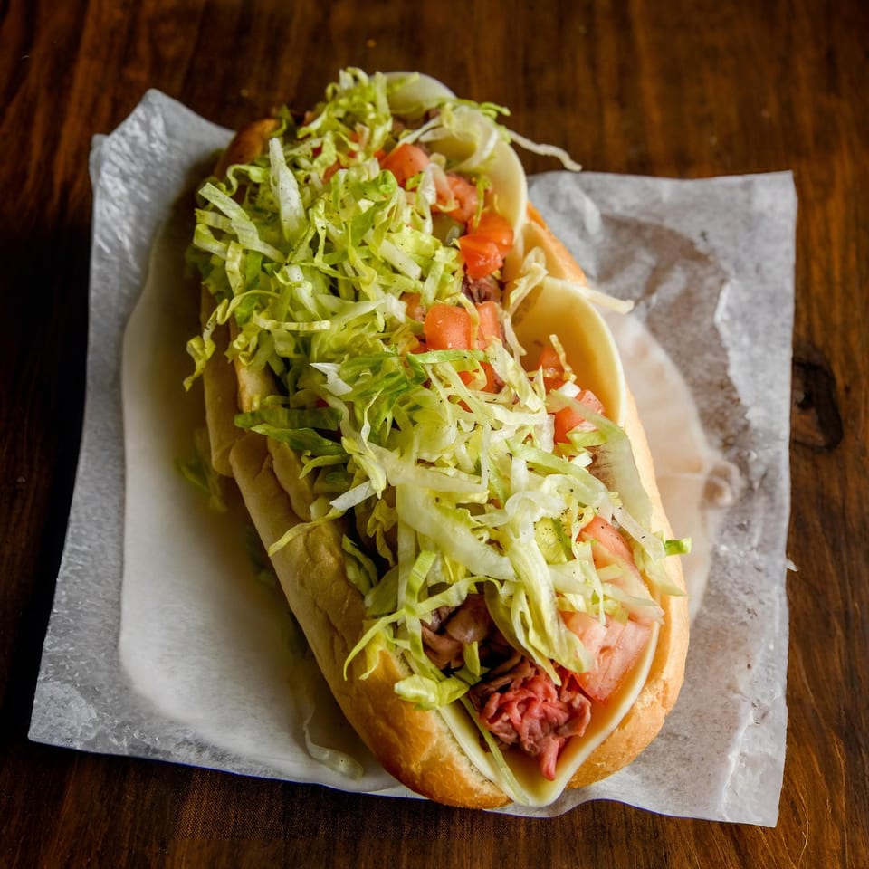 A Nicolini House of Pizza sub sandwich with meat, cheese, lettuce, and tomatoes on a wooden table.