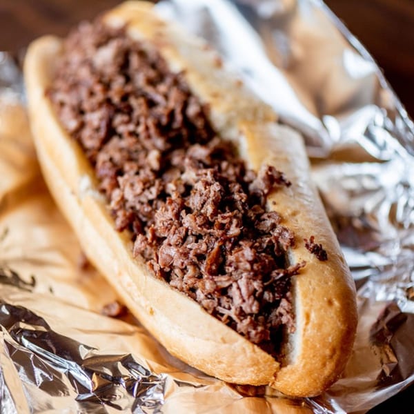 A Nicolini House of Pizza cheesesteak sandwich, filled with thinly sliced meat, resting on foil.