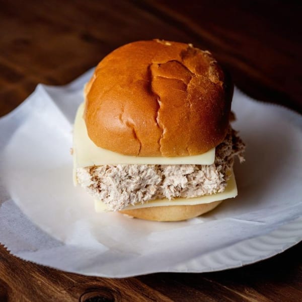 A tuna salad sandwich with cheese on a bun, served on a white paper plate.
