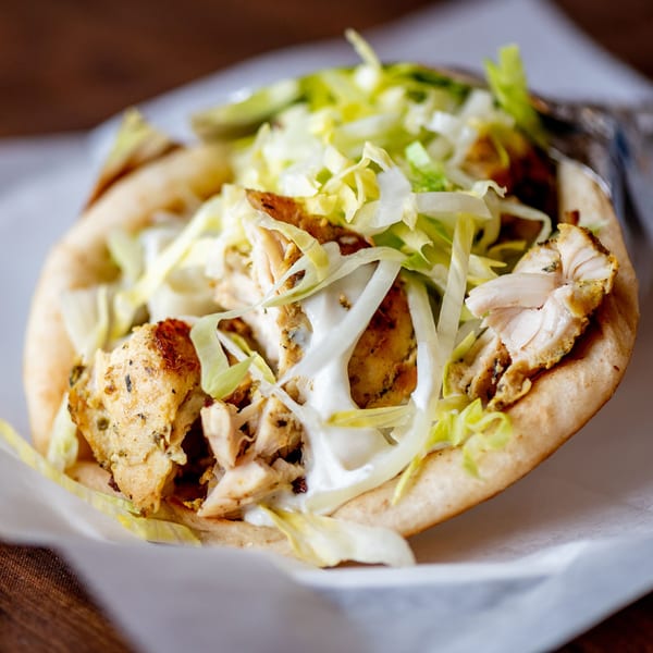 A close-up of a chicken gyro from Nicolini House of Pizza, filled with chicken, lettuce, and sauce.
